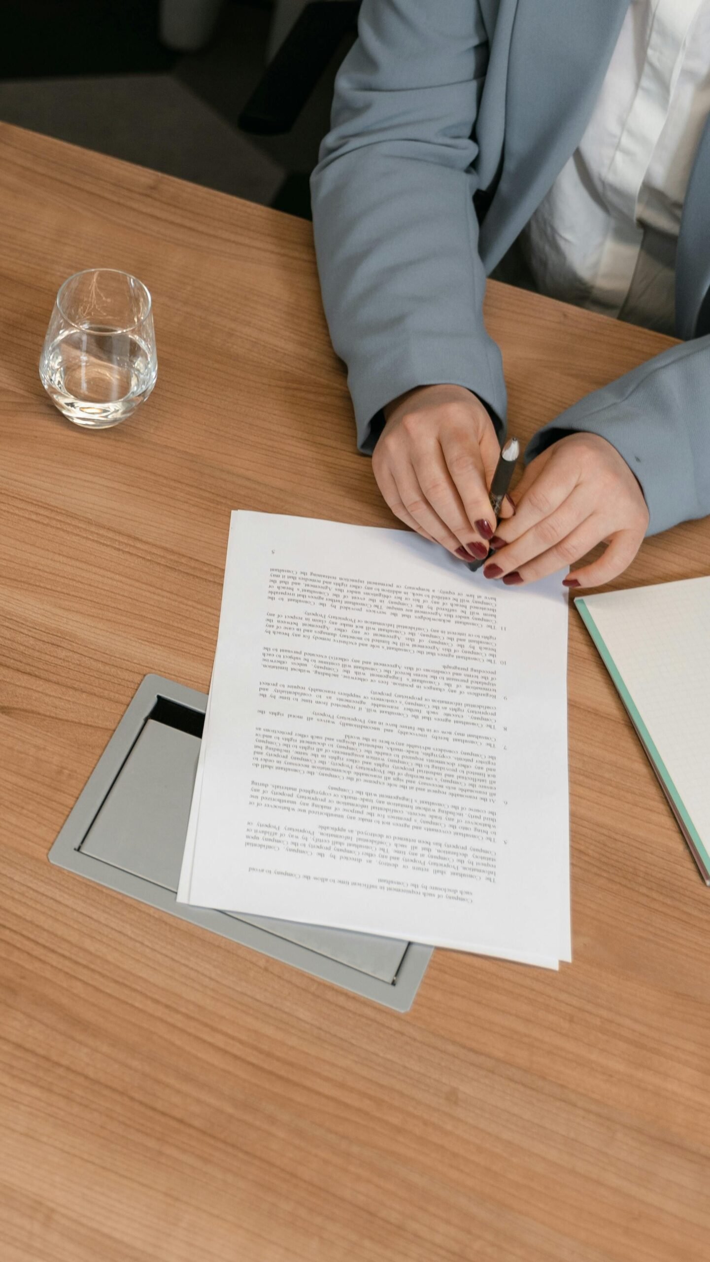 A person's hands rest over a piece of paper while holding a pen and considering online writing programs.